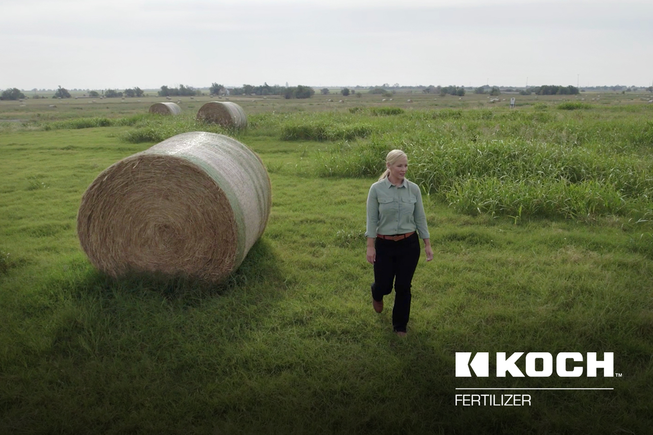 Woman standing in field beside hay bale